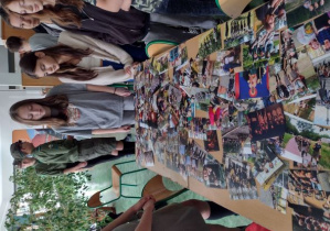 Uczniowie stojący przy zdjęciach leżących na stoliku.